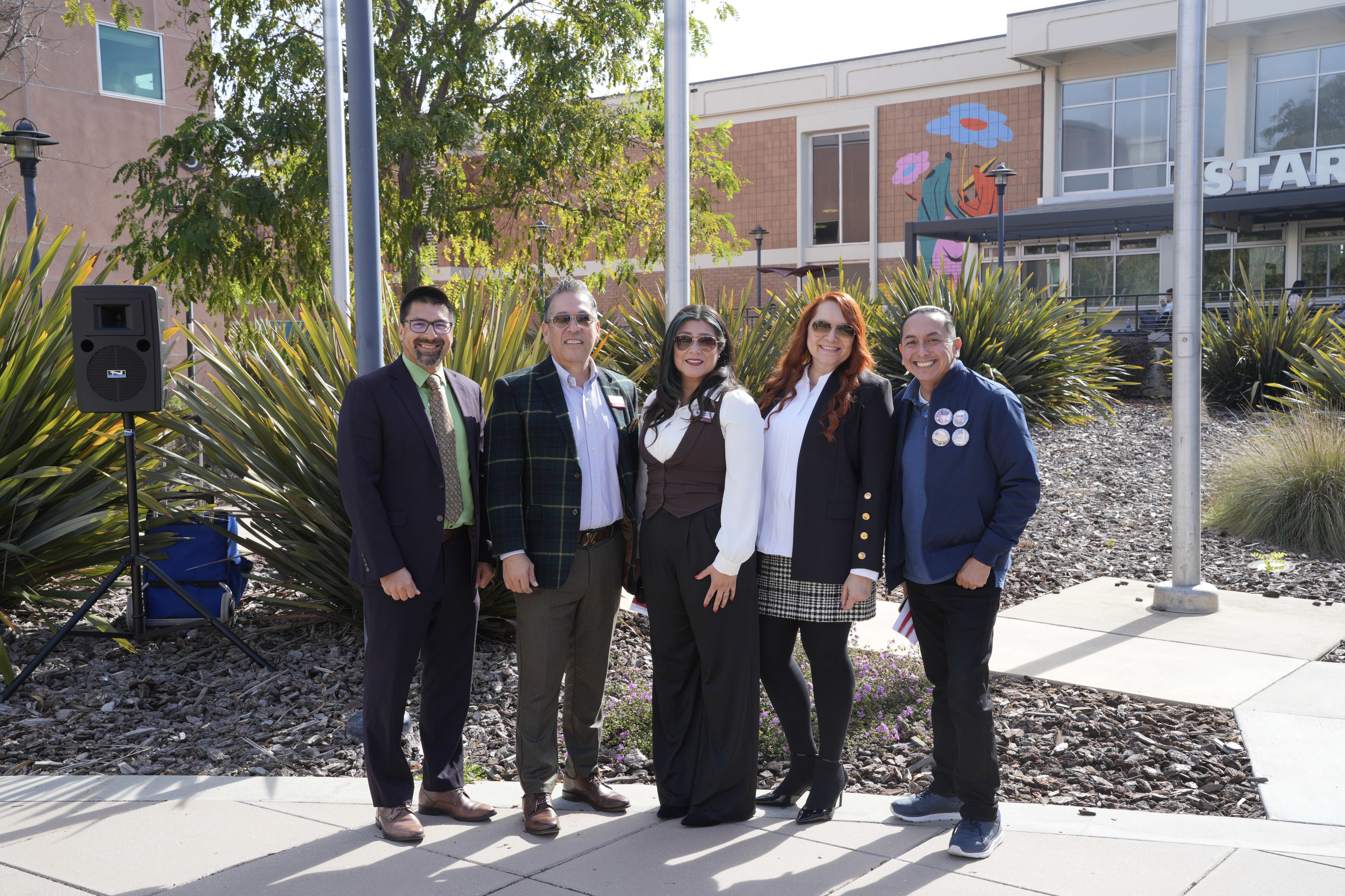 Five people, including community leaders, stand together smiling outdoors in front of a Starbucks and colorful mural.